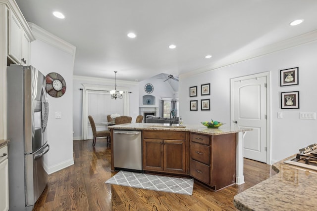 kitchen featuring dark wood-style floors, appliances with stainless steel finishes, crown molding, a fireplace, and a sink