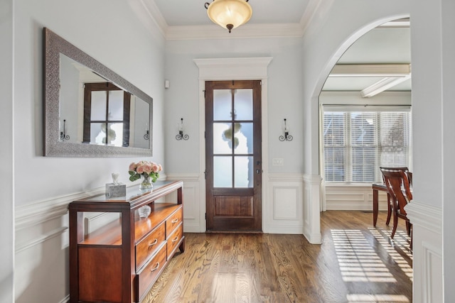 entrance foyer with ornamental molding, arched walkways, wood finished floors, and wainscoting