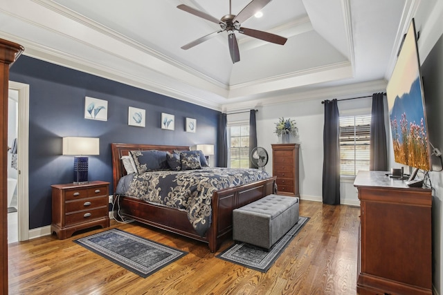 bedroom with baseboards, ornamental molding, a raised ceiling, and wood finished floors