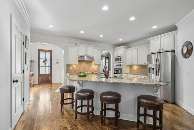 kitchen with under cabinet range hood, arched walkways, stainless steel appliances, and a sink