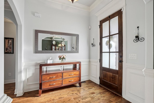 entrance foyer with ornamental molding, arched walkways, a wainscoted wall, and light wood finished floors