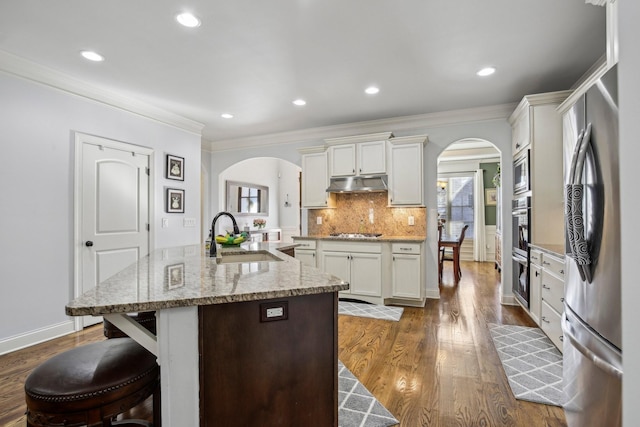 kitchen with under cabinet range hood, arched walkways, stainless steel appliances, and a sink