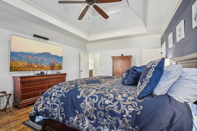 bedroom with a ceiling fan, a tray ceiling, crown molding, and wood finished floors