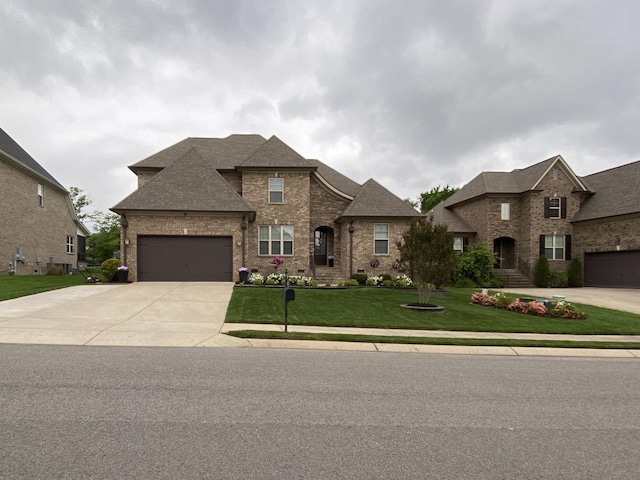 french country inspired facade with an attached garage, brick siding, a shingled roof, driveway, and a front lawn