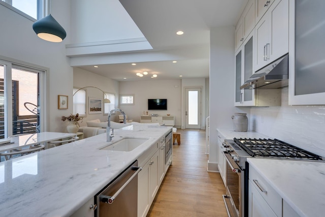 kitchen featuring under cabinet range hood, a sink, light wood-style floors, open floor plan, and appliances with stainless steel finishes