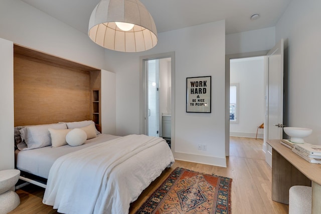 bedroom with ensuite bathroom, light wood-style flooring, and baseboards