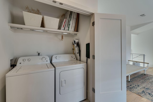 clothes washing area with washer and dryer, laundry area, visible vents, and light wood-style flooring