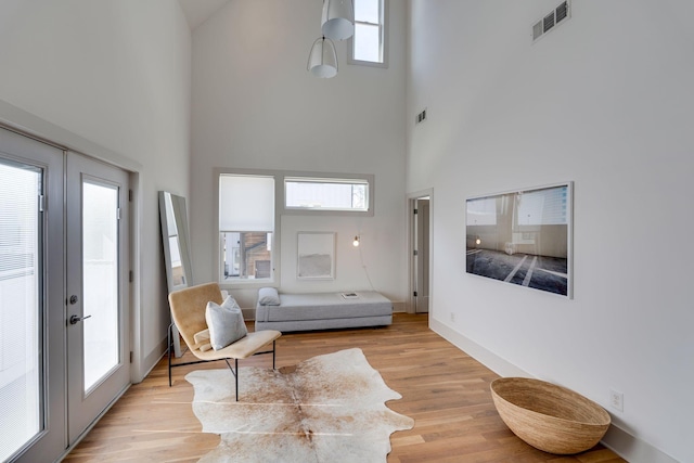 living room with visible vents, baseboards, a towering ceiling, light wood-style flooring, and french doors