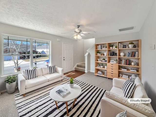 carpeted living area with stairway, a ceiling fan, visible vents, and a textured ceiling