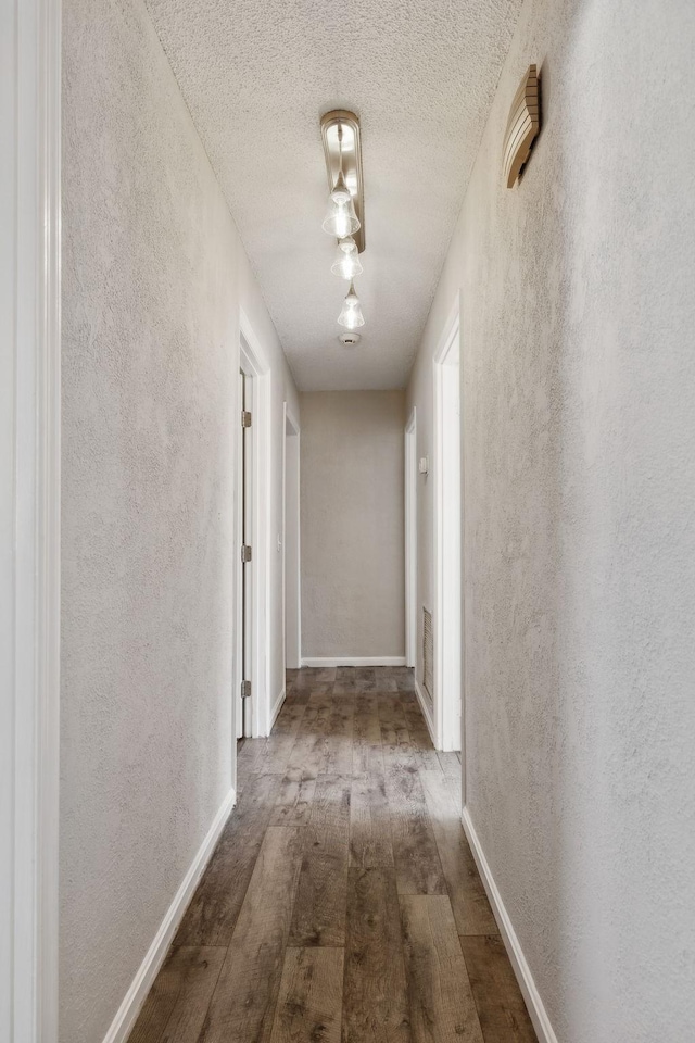 corridor featuring a textured ceiling, baseboards, wood finished floors, and a textured wall