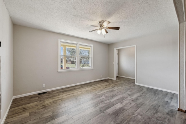 spare room with baseboards, visible vents, ceiling fan, wood finished floors, and a textured ceiling