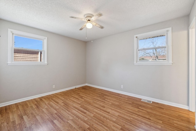 unfurnished room with light wood-style flooring, a textured ceiling, visible vents, and baseboards