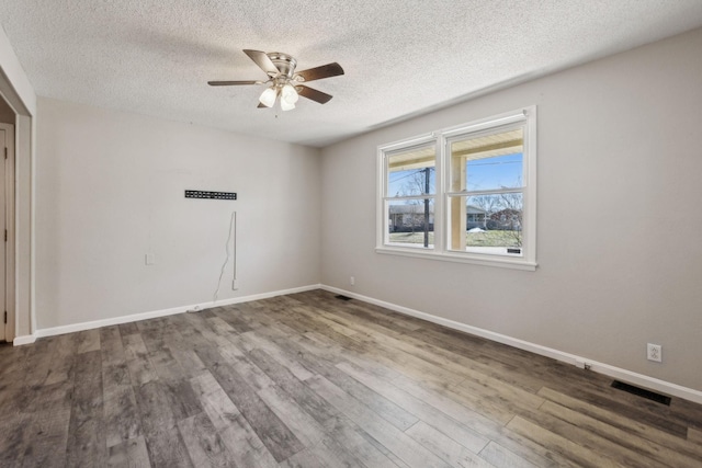 empty room with a textured ceiling, wood finished floors, a ceiling fan, visible vents, and baseboards