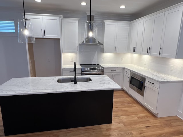 kitchen featuring light wood finished floors, wall chimney exhaust hood, light stone counters, stainless steel appliances, and a sink