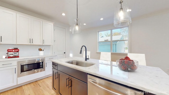 kitchen with decorative light fixtures, stainless steel appliances, light wood-style flooring, white cabinetry, and a sink