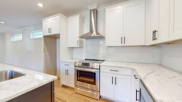 kitchen with light stone counters, white cabinetry, wall chimney range hood, and stainless steel electric range