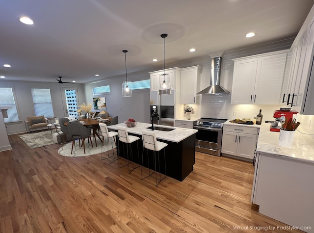 kitchen with appliances with stainless steel finishes, light wood-style floors, a sink, and wall chimney range hood