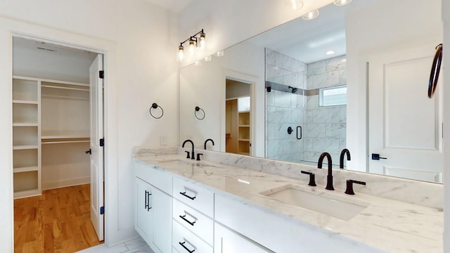 bathroom featuring a walk in closet, a sink, a shower stall, and double vanity