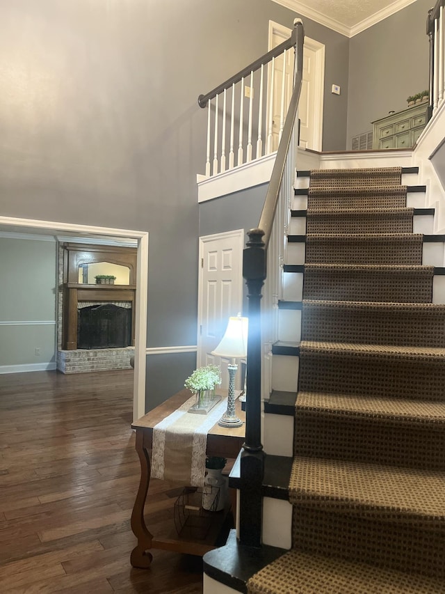 stairs with baseboards, ornamental molding, wood finished floors, a high ceiling, and a fireplace