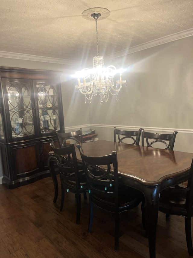 dining space featuring an inviting chandelier, a textured ceiling, ornamental molding, and dark wood-type flooring