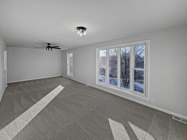 spare room featuring a ceiling fan, dark carpet, visible vents, and baseboards