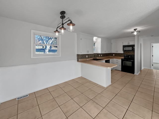 kitchen featuring light tile patterned floors, a peninsula, a sink, black appliances, and tasteful backsplash