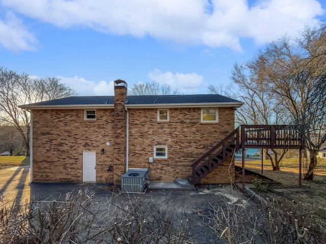 back of house featuring brick siding, a chimney, stairway, central AC unit, and a wooden deck