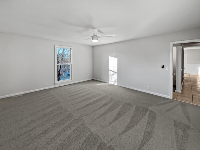 carpeted empty room with baseboards, visible vents, and a ceiling fan