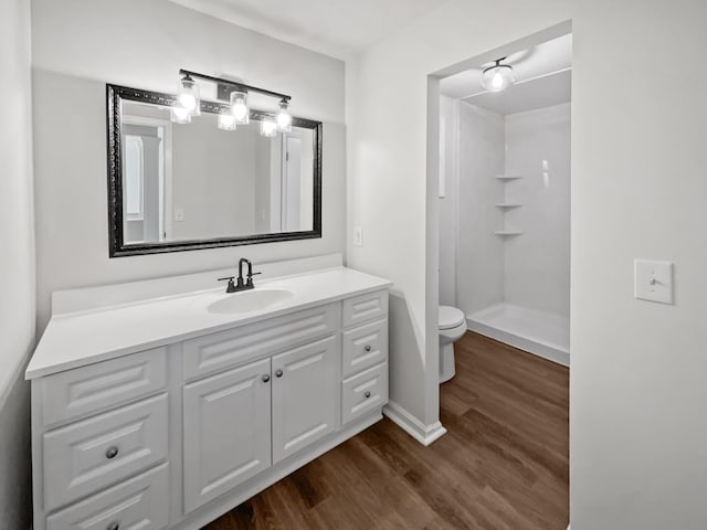 full bath featuring toilet, wood finished floors, vanity, baseboards, and walk in shower