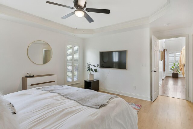 bedroom with baseboards, ceiling fan, a tray ceiling, crown molding, and light wood-type flooring