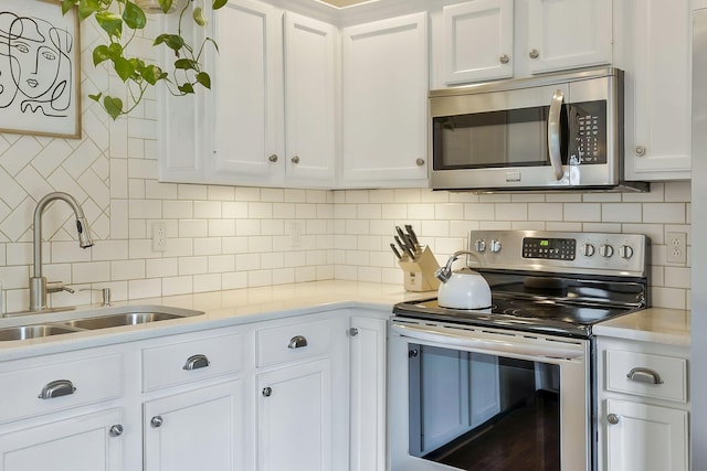 kitchen with tasteful backsplash, white cabinets, appliances with stainless steel finishes, light countertops, and a sink