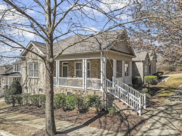 view of front facade with roof with shingles, a porch, and brick siding