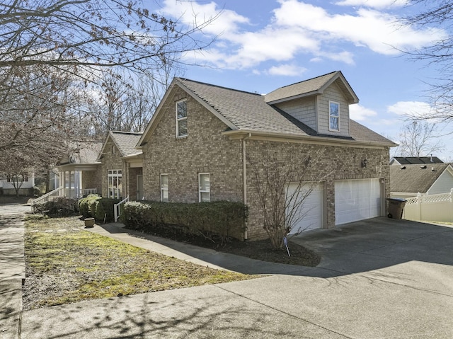 view of side of property with driveway, a garage, a shingled roof, fence, and brick siding