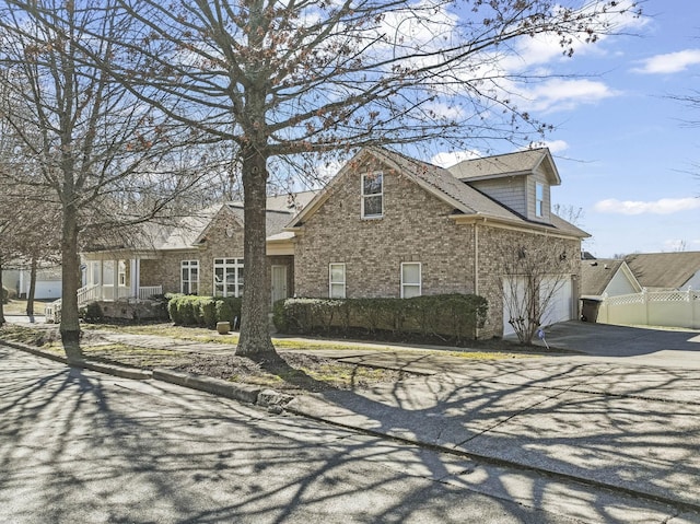 view of front of home featuring a garage, brick siding, driveway, and fence