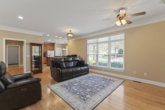 living area with ornamental molding, light wood-style flooring, visible vents, and baseboards