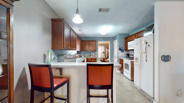 kitchen with white appliances, visible vents, a breakfast bar, decorative light fixtures, and a peninsula