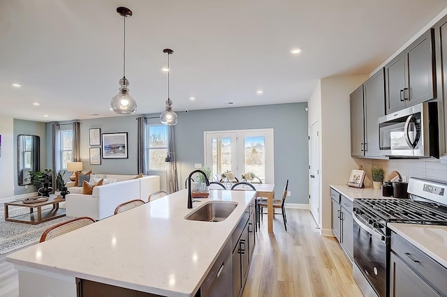 kitchen featuring a kitchen island with sink, stainless steel appliances, a sink, light wood-type flooring, and decorative backsplash