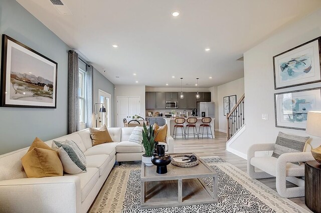 living area featuring baseboards, stairway, light wood-type flooring, and recessed lighting