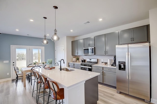 kitchen with a kitchen island with sink, gray cabinetry, stainless steel appliances, a breakfast bar, and a sink