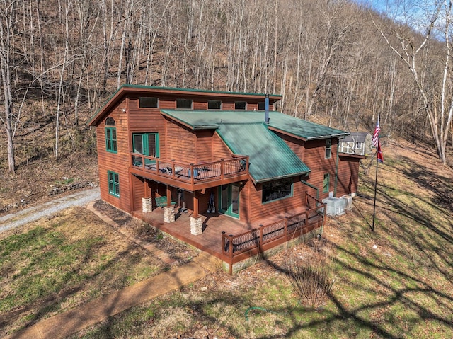 back of house featuring driveway, a deck, metal roof, and a yard