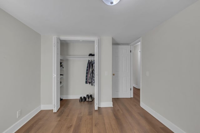 unfurnished bedroom with a closet, wood finished floors, and baseboards