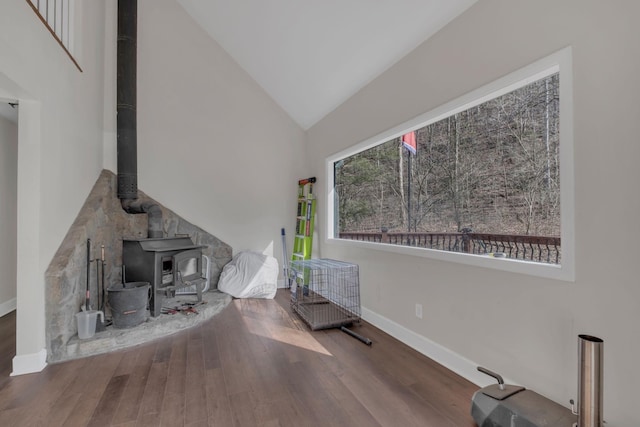 living area featuring a wood stove, high vaulted ceiling, baseboards, and wood finished floors