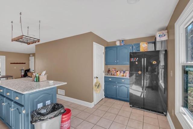 kitchen with light tile patterned floors, blue cabinetry, freestanding refrigerator, and baseboards