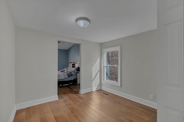 unfurnished room with visible vents, baseboards, and hardwood / wood-style floors