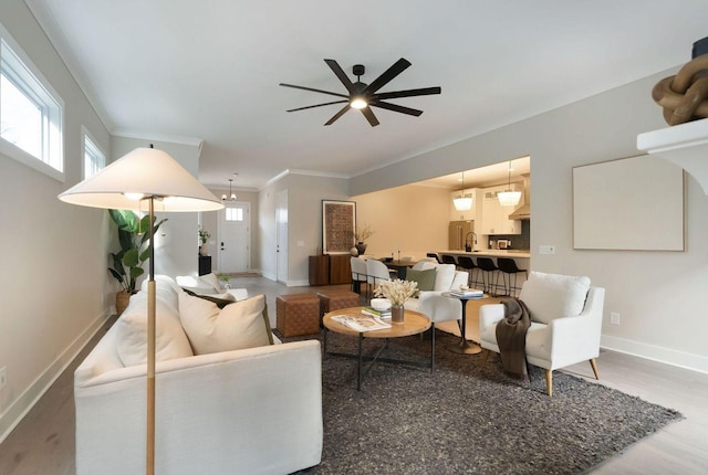 living area with baseboards, ceiling fan, light wood-type flooring, and crown molding