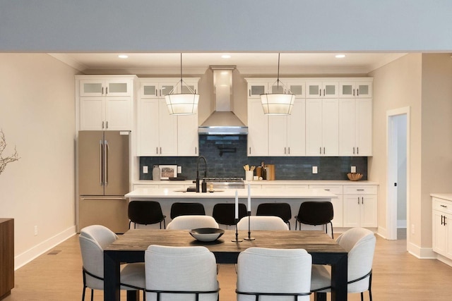 kitchen with an island with sink, wall chimney exhaust hood, light countertops, and high end fridge