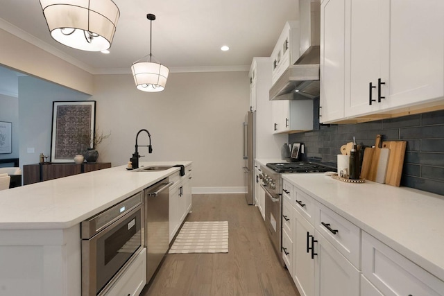 kitchen featuring premium appliances, a sink, wall chimney range hood, tasteful backsplash, and crown molding