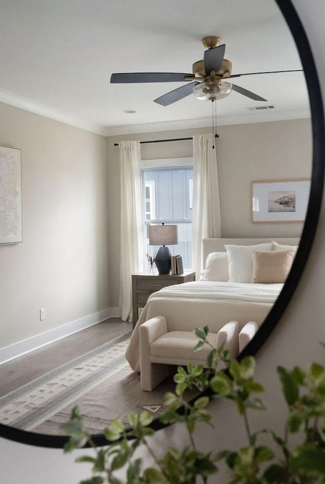 bedroom with ceiling fan, wood finished floors, visible vents, baseboards, and crown molding