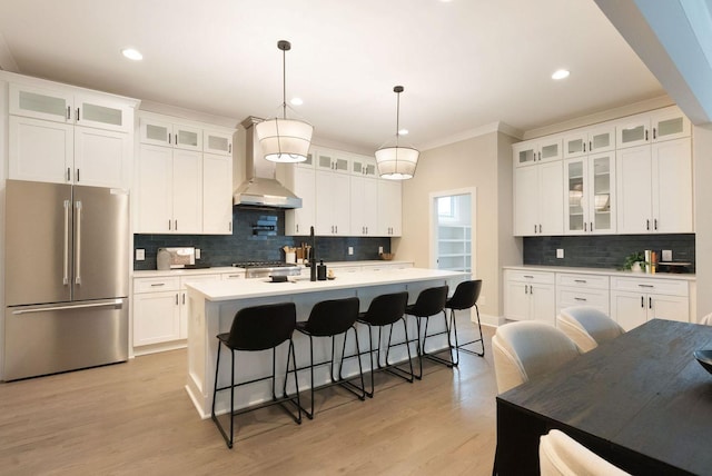 kitchen with an island with sink, wall chimney exhaust hood, light wood-style flooring, light countertops, and high end fridge