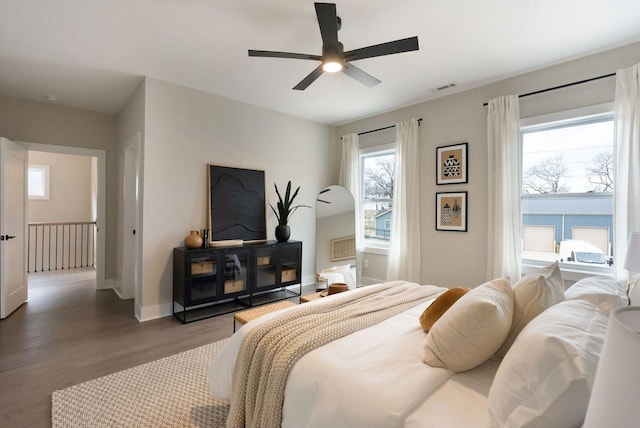 bedroom with a ceiling fan, wood finished floors, visible vents, and baseboards